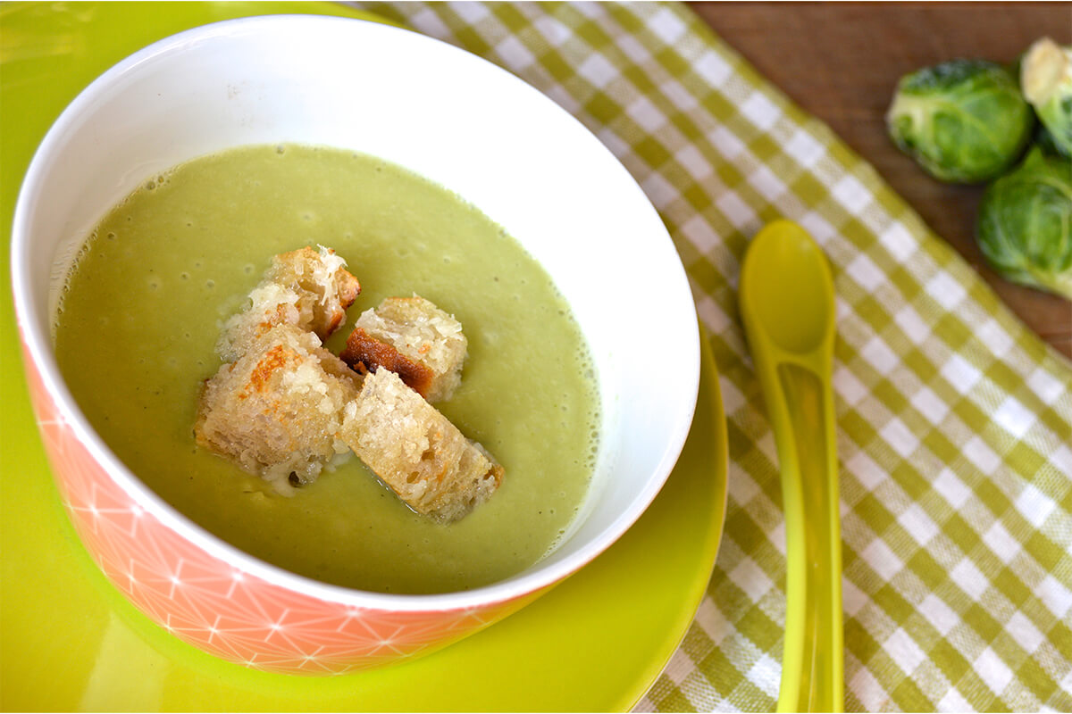 A bowl of Sprout Soup With Cheesy Croutons next to some Brussels sprouts