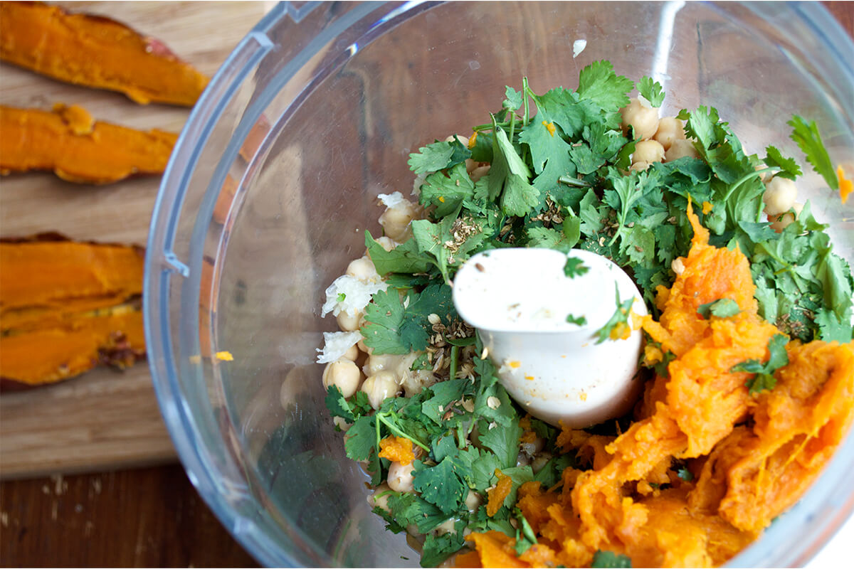 A food processor with sweet potato, garlic, coriander, chickpeas and herbs