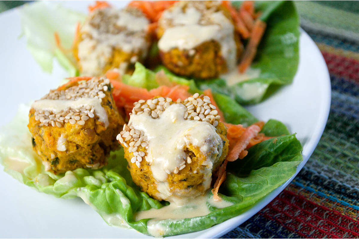 Sweet potato falafels served on lettuce leaves with grated carrot and drizzled with tahini dressing