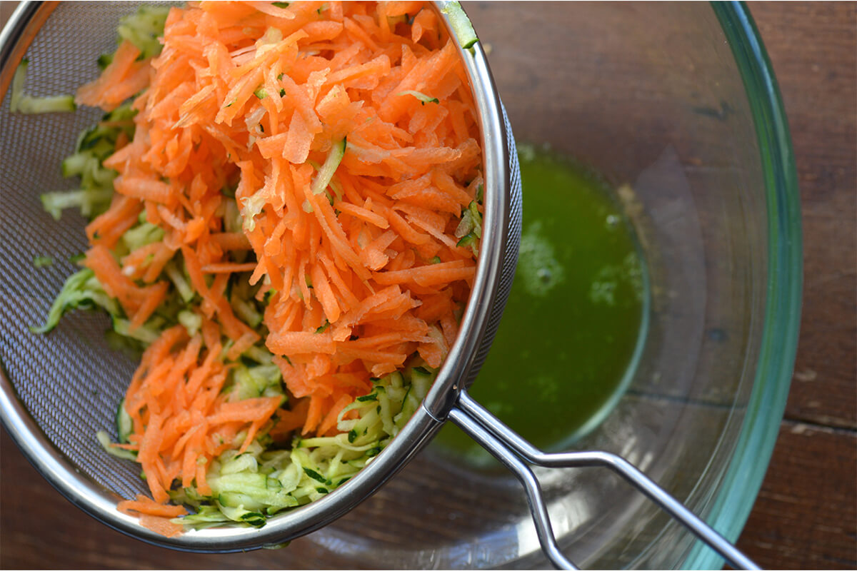 Grated carrot and courgette in a sieve draining over a glass bowl