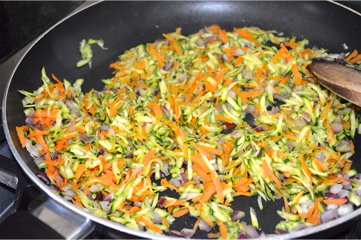 Onion, grated courgette and carrot being fried in frying pan