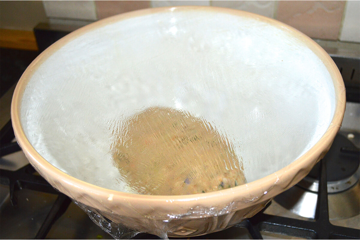 Vegetable Bread dough in a large mixing bowl covered with cling film