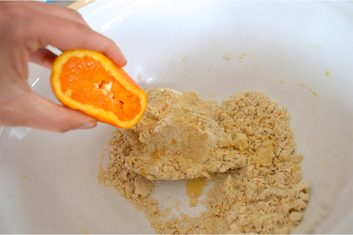 A mixing bowl with tart pastry with a halved orange being squeezed into it