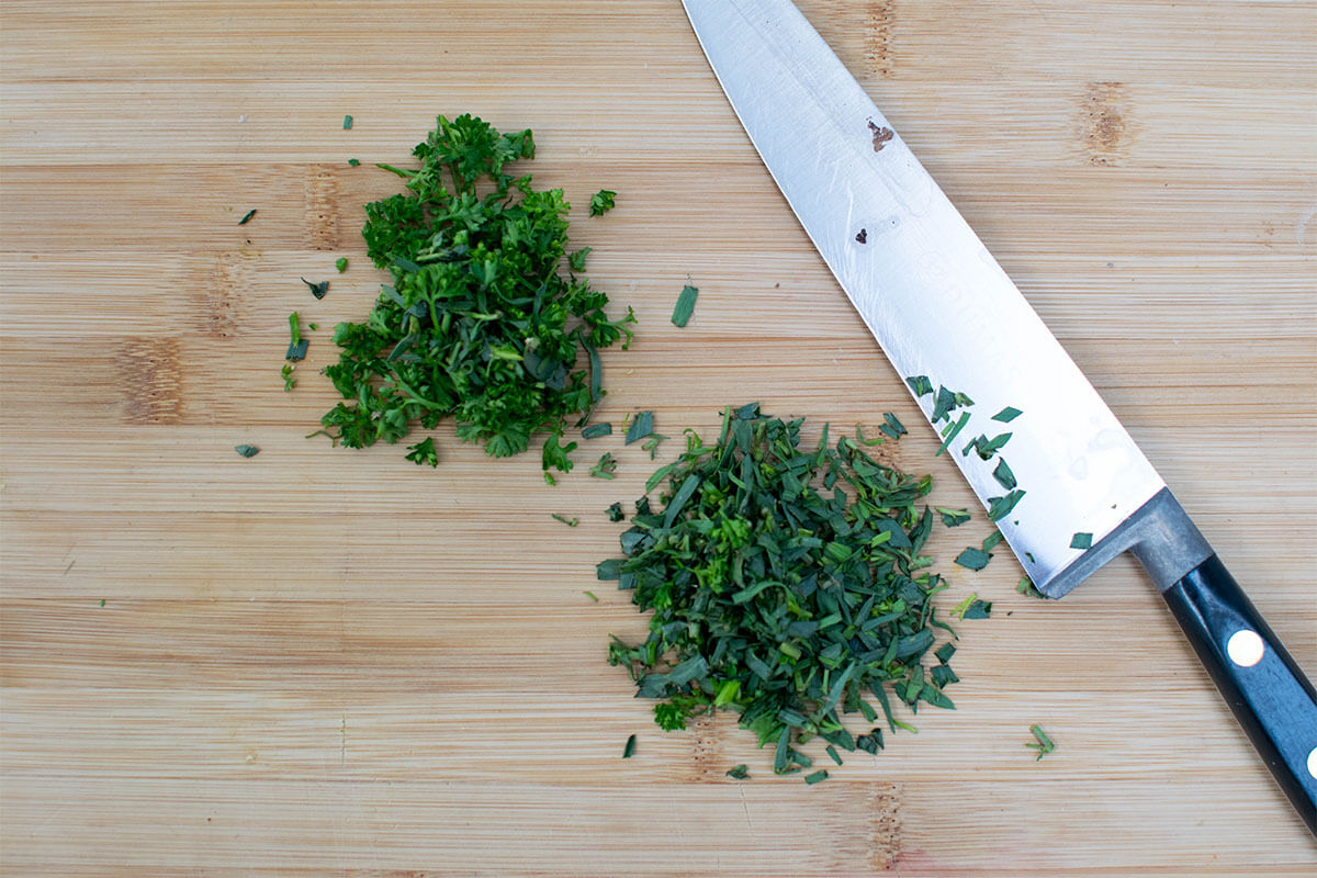 A chopping board with chopped tarragon and parsley