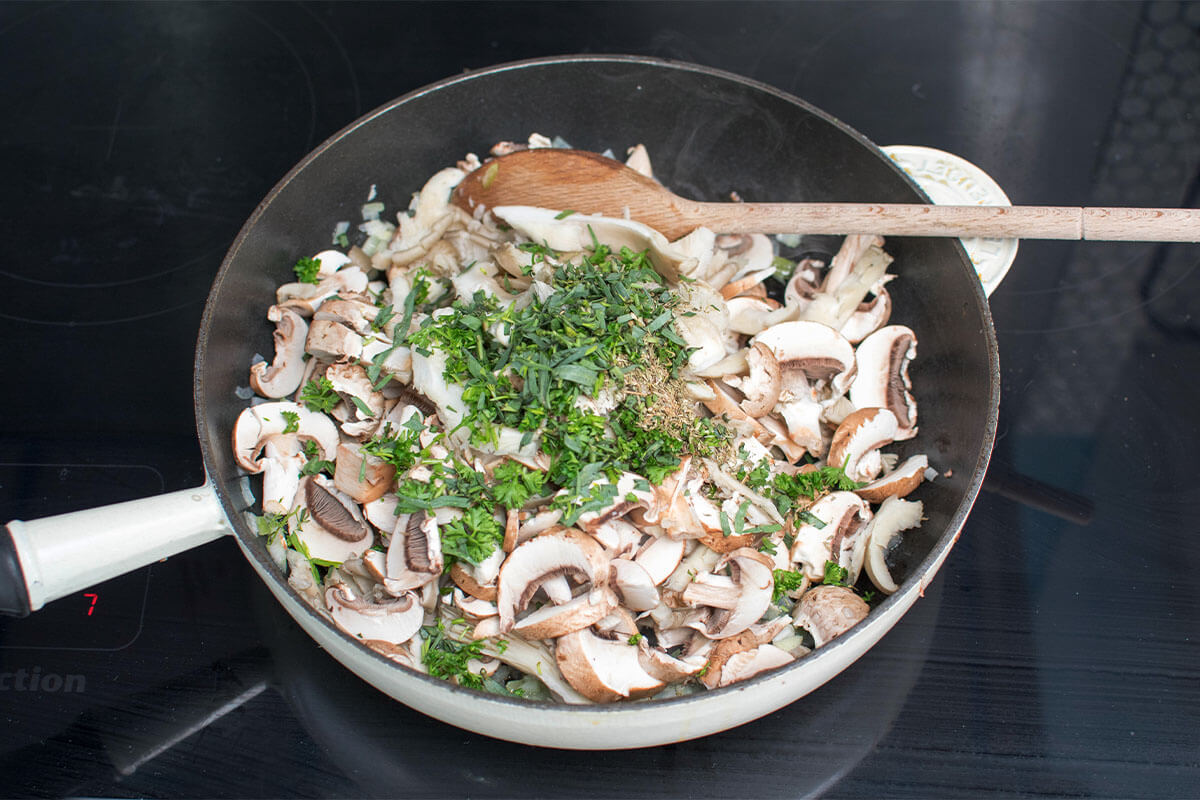 A frying pan with chopped onion, garlic, mushroom and herbs