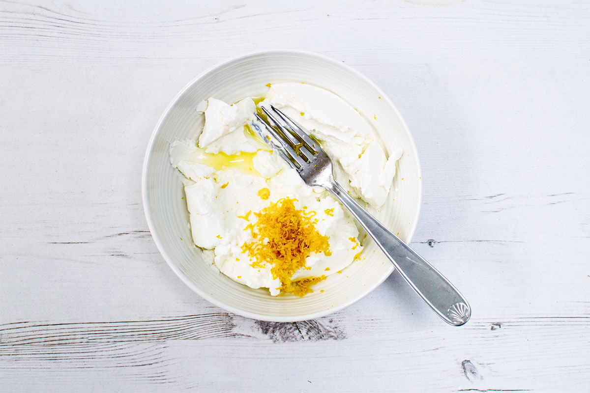 A bowl or ricotta being mixed with lemon juice and zest