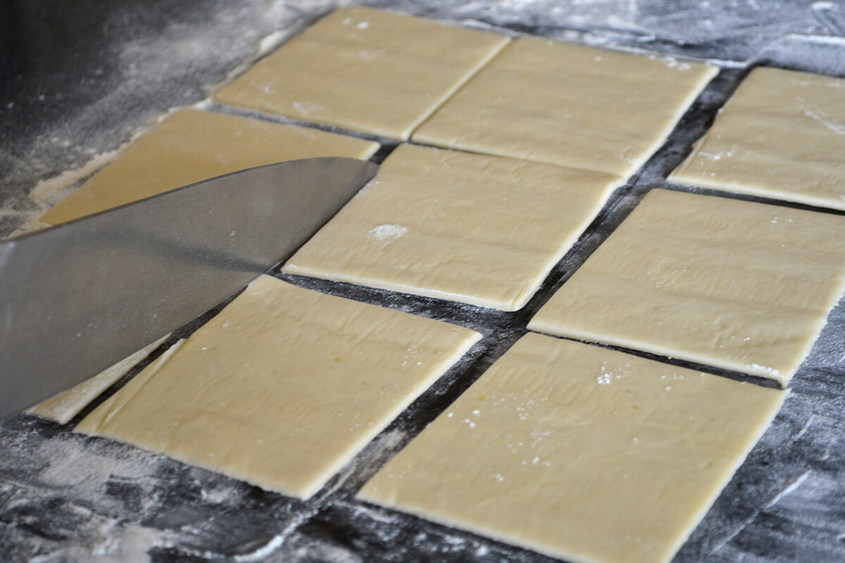 Pastry being cut into squares on a floured surface