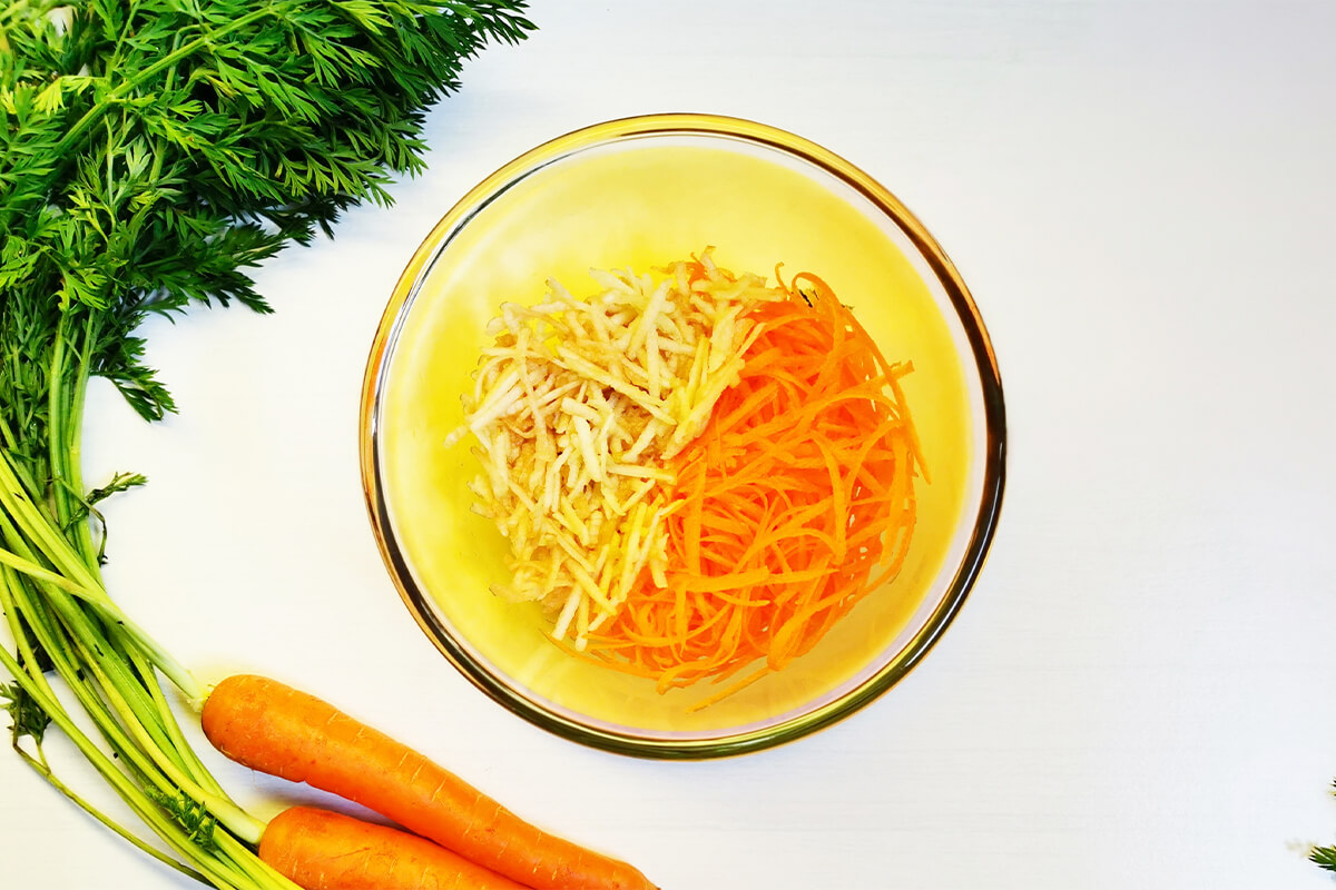 A bowl of grated carrot and apple, next to some carrots