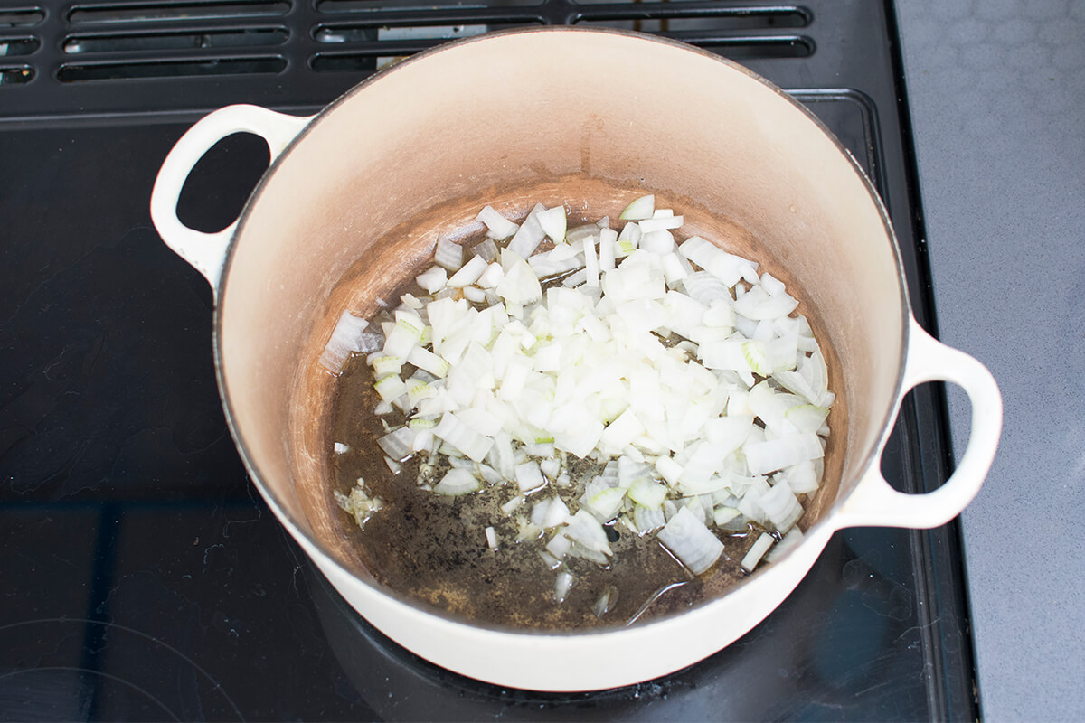 A large pan with finely chopped onion and crushed garlic being fried in oil