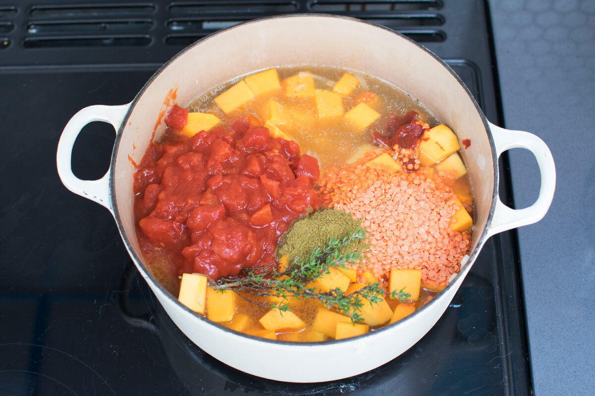 A large pan with finely chopped onion, garlic, diced butternut squash, lentils, tomato puree and chopped tomatoes, fresh thyme, stock and ground cumin