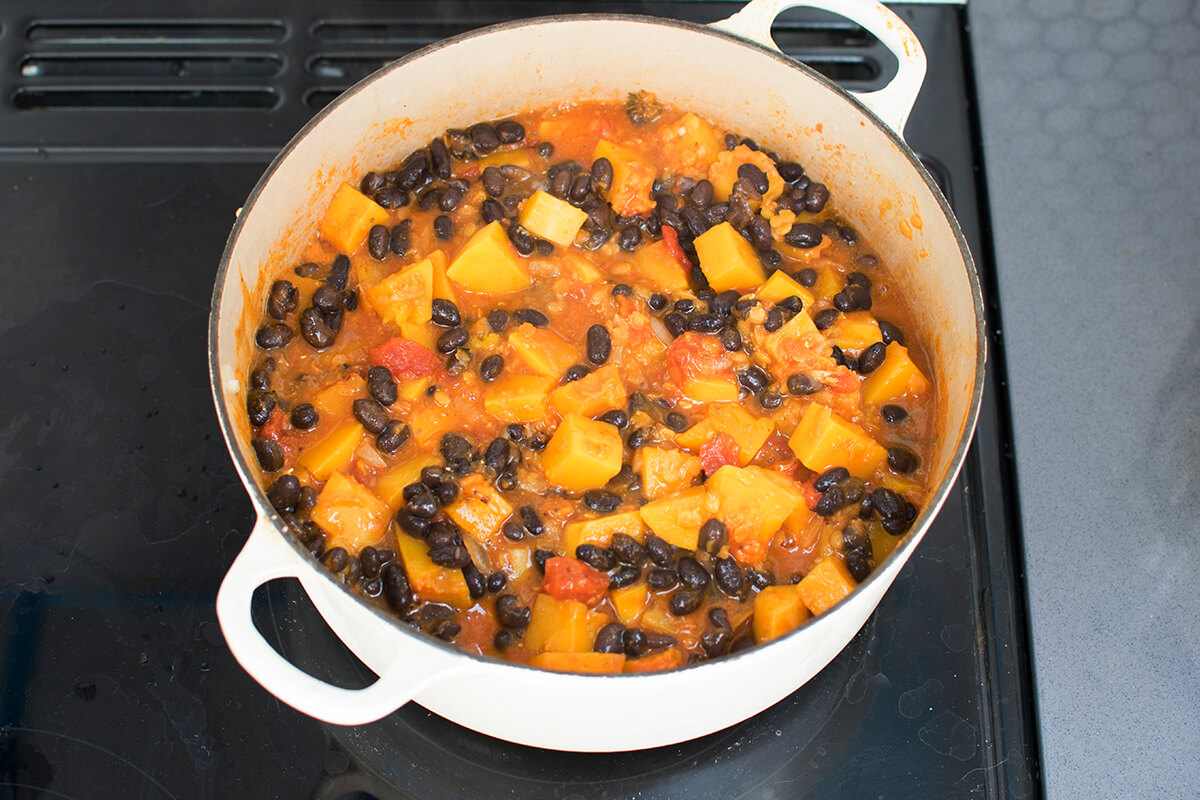 A large pan with finely chopped onion, garlic, diced butternut squash, lentils, tomato puree and chopped tomatoes, fresh thyme, stock, ground cumin and black beans