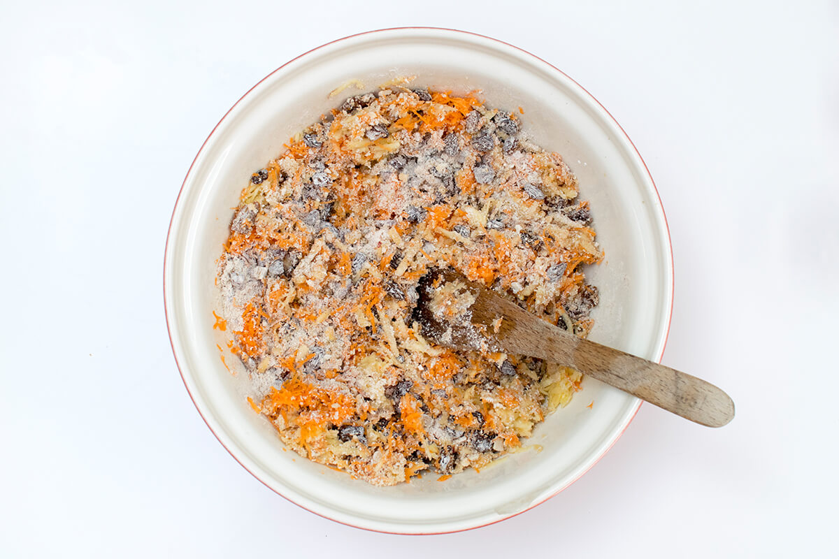 A bowl of flour, breadcrumbs, ground mixed spice, cinnamon, raisins and dates with orange juice and zest, grated frozen butter, beaten eggs and milk