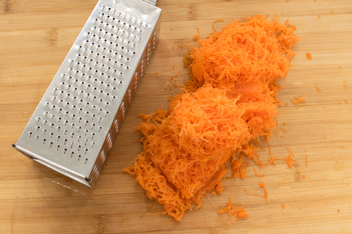 A chopping board with grated carrot next to a grater