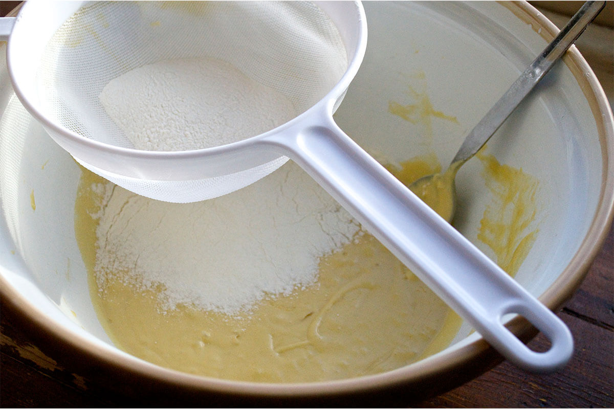 A bowl of cupcake batter with flour being sifted into it