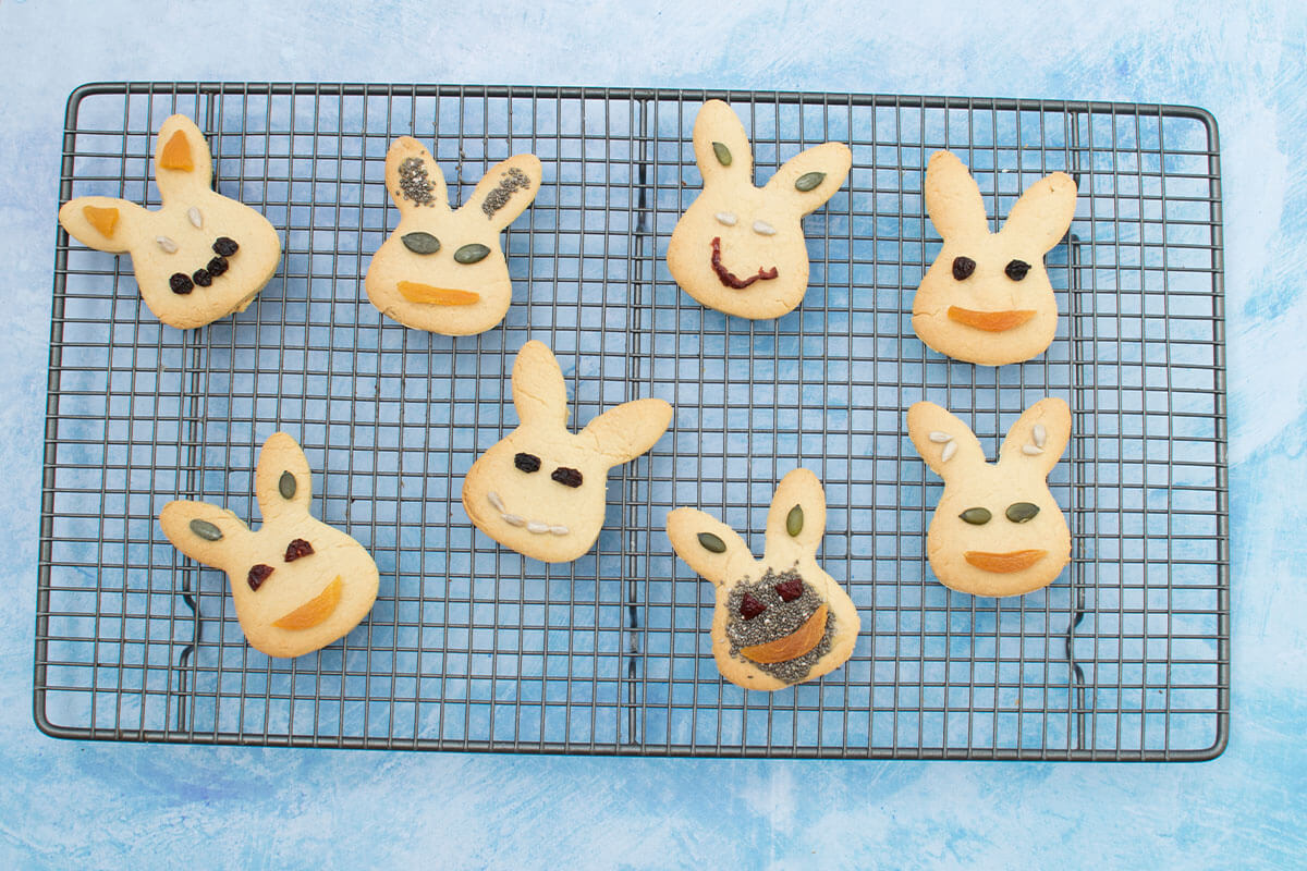 A cooling rack with 9 bunny shaped biscuits decorated with dried fruit and seeds