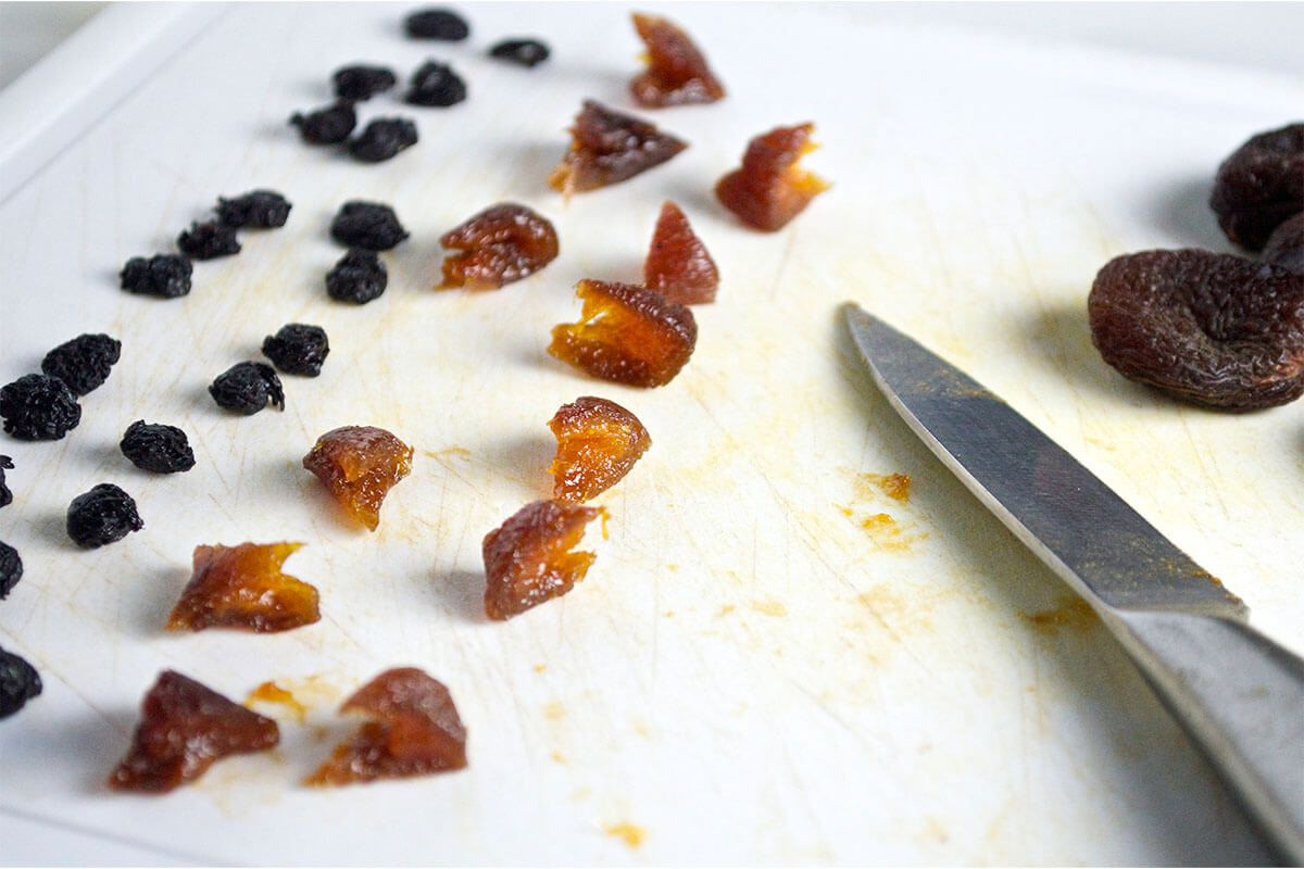 A chopping board with raisins and chopped dried apricots