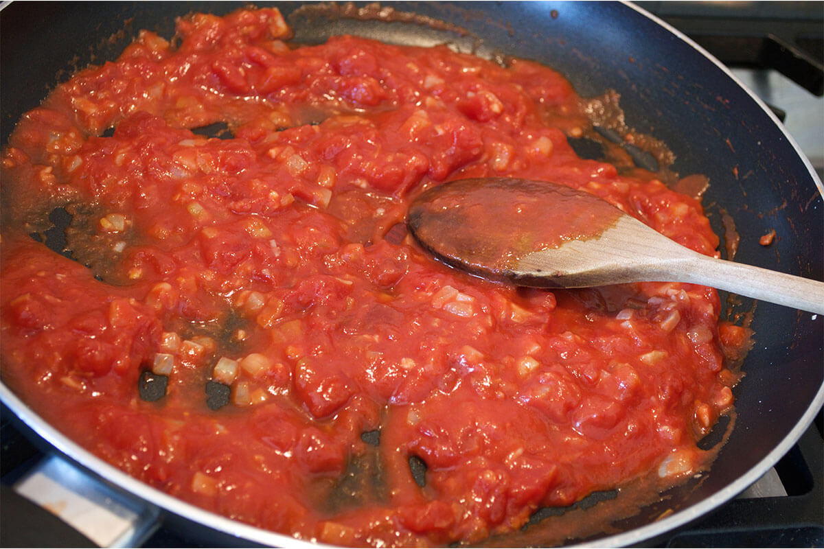 A frying pan with chopped onion, tinned tomatoes and tomato puree