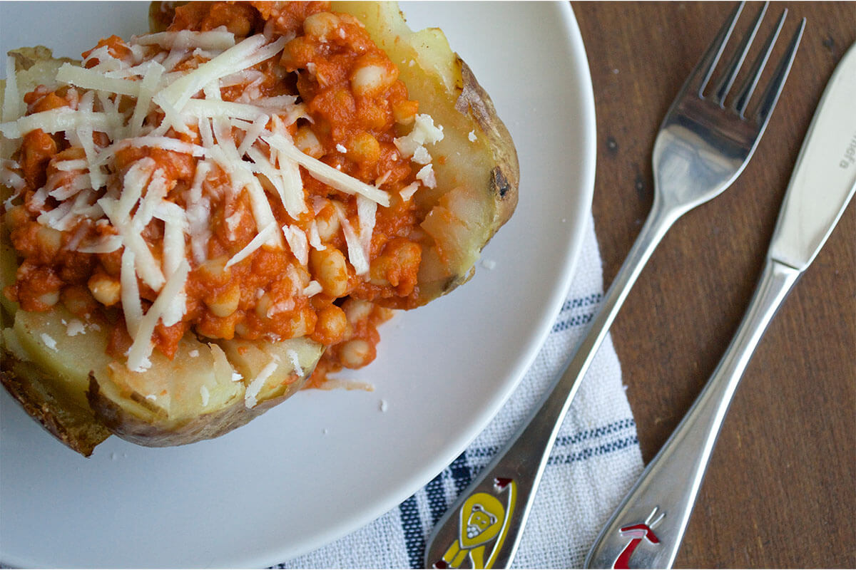 A serving of jacket potato topped with homemade baked beans and grated cheese