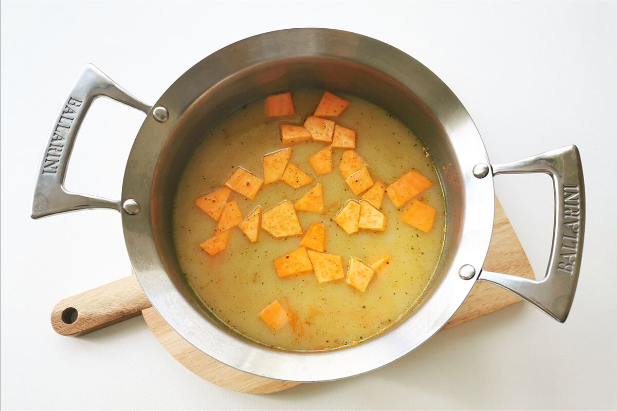 A saucepan with diced onion, garlic and cumin with added carrots, lentils, sweet potato, vegetable stock and milk