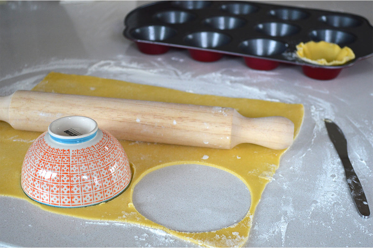 A floured surface with pastry being rolled out and cut using a bowl