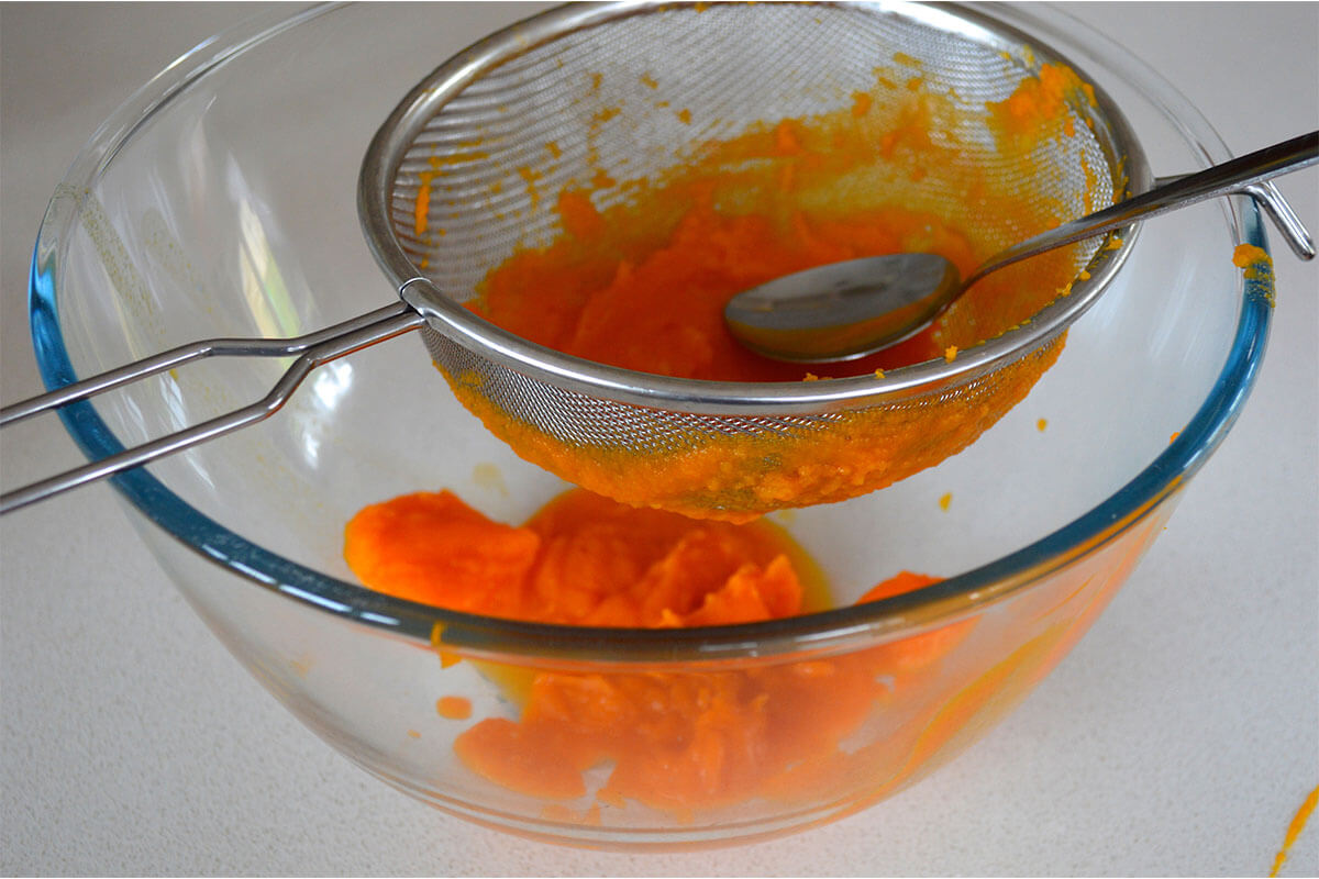 Pumpkin being sieved over a glass bowl