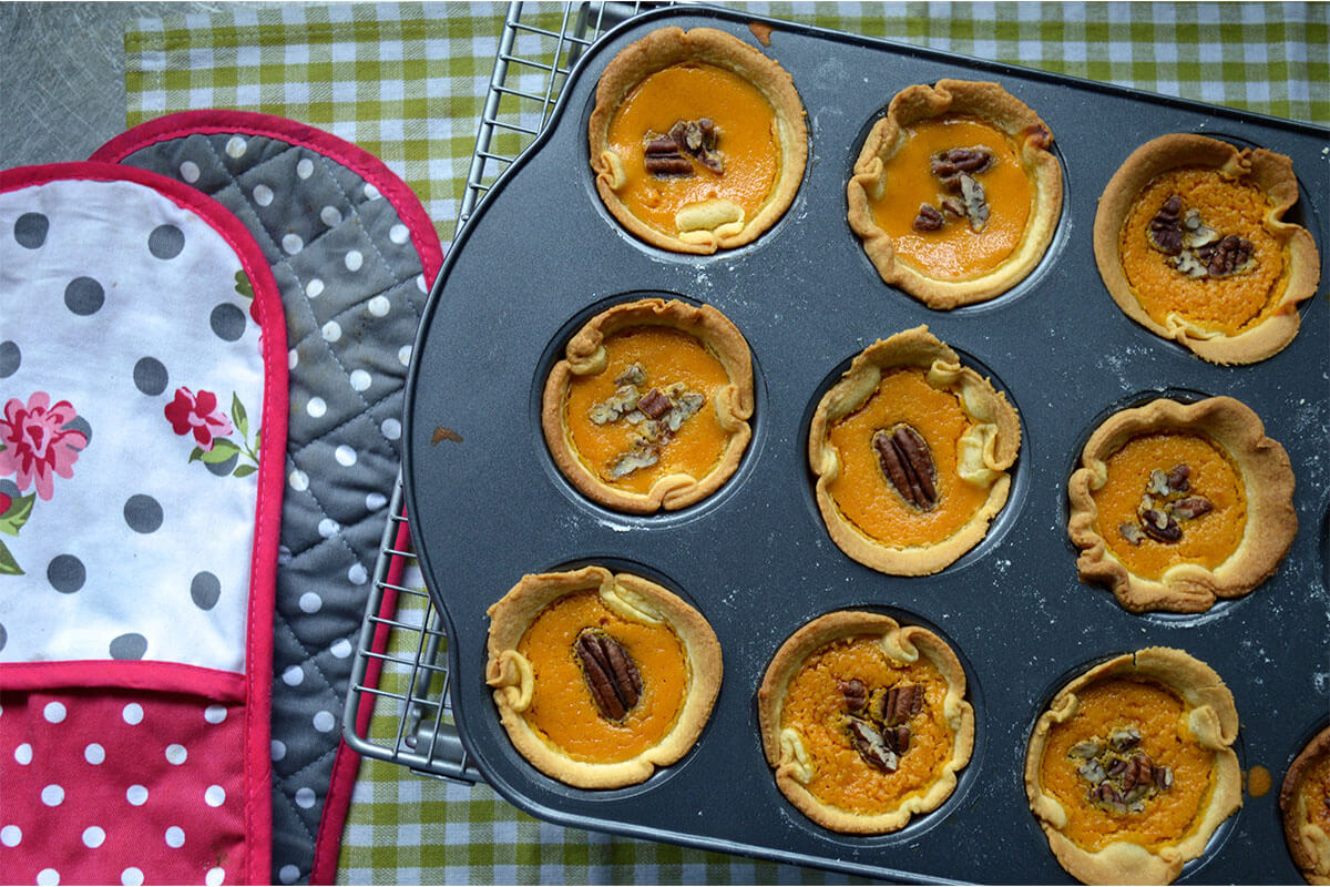 A cupcake tin of Mini Maple & Pumpkin Pies topped with pecans
