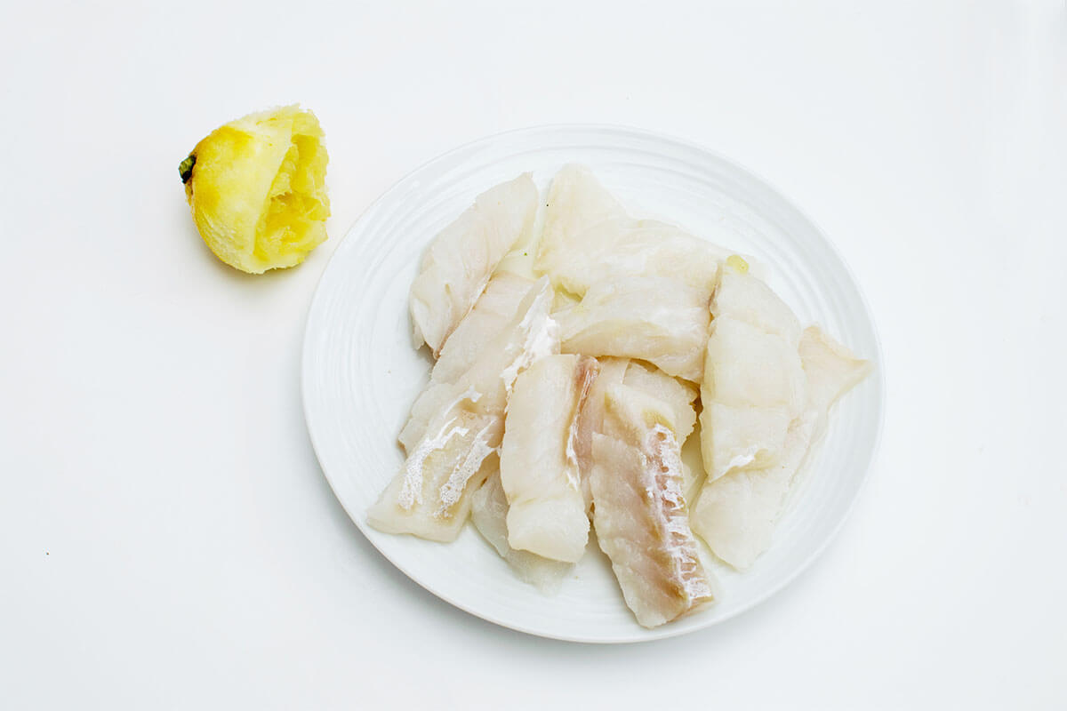 A plate of chunky fillet strips next to a halved, zested and juiced, lemon