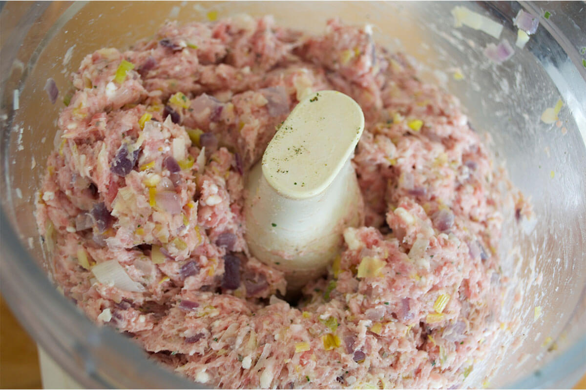 A food processor with leek, red onion, feta, parmesan, herbs and pork mince