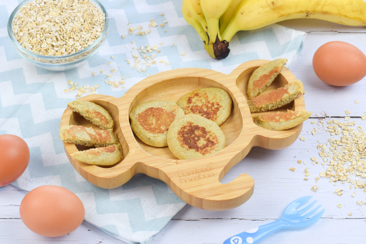 A serving of oat pancakes next to a bowl of oats, some eggs and a bunch of bananas