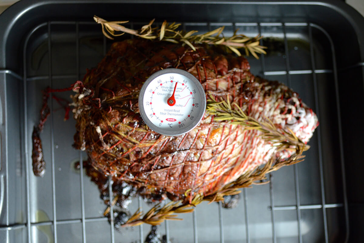 Lamb tied with string, on a roasting tray and being checked with a cooking thermometer