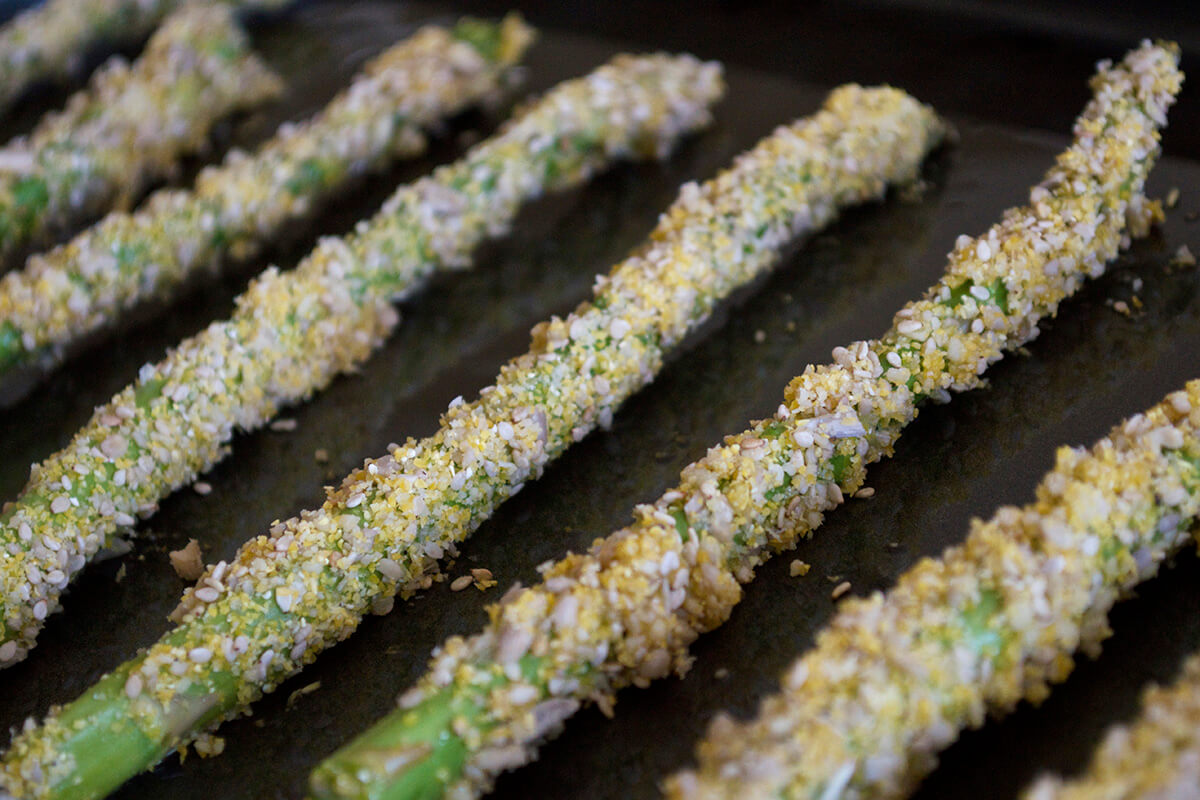 Asparagus, coated in egg and seed mix, on a baking tray