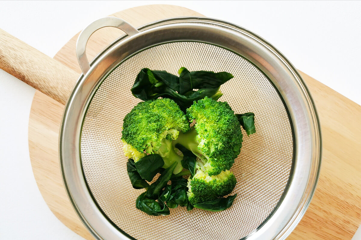 Broccoli florets and spinach leaves in a sieve