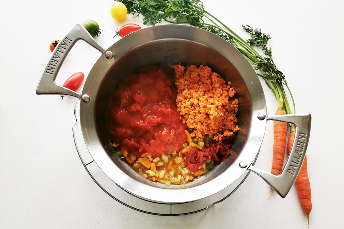 A pan of chopped onion, crushed garlic, carrots and celery with lentils, tinned tomatoes, tomato puree and vegetable stock