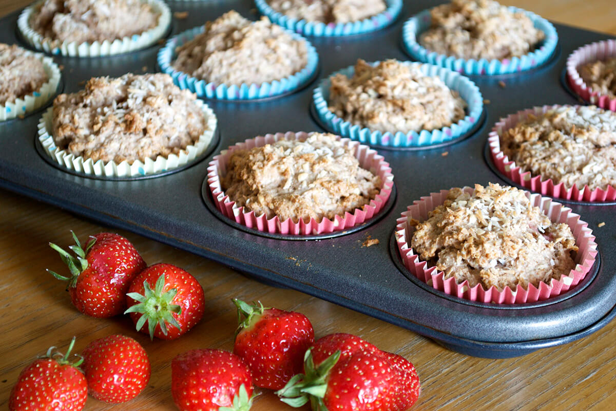 Baby Strawberry Muffins in a muffin tray next to some strawberries