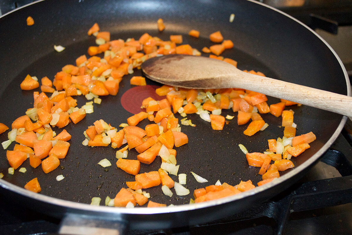 Finely chopped onion and carrot being softened in a saucepan