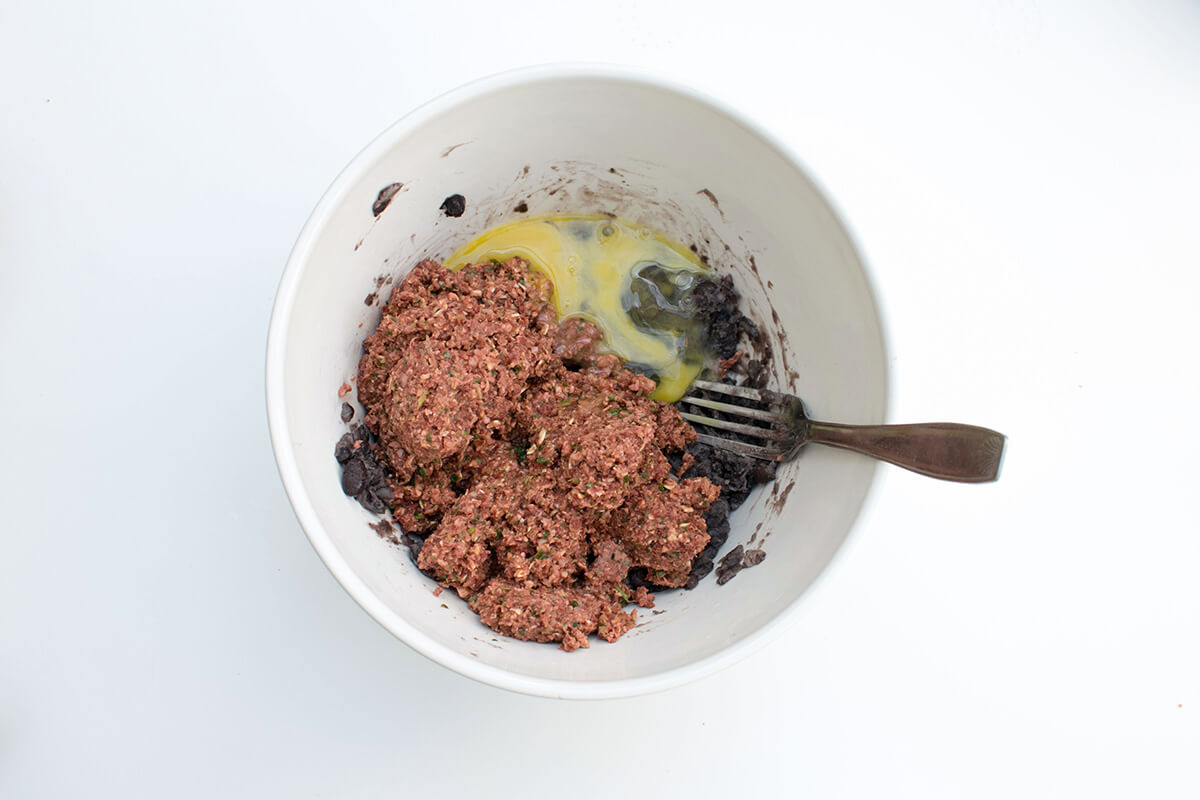 A bowl of blended beetroot burger mix with mashed black beans and a beaten egg