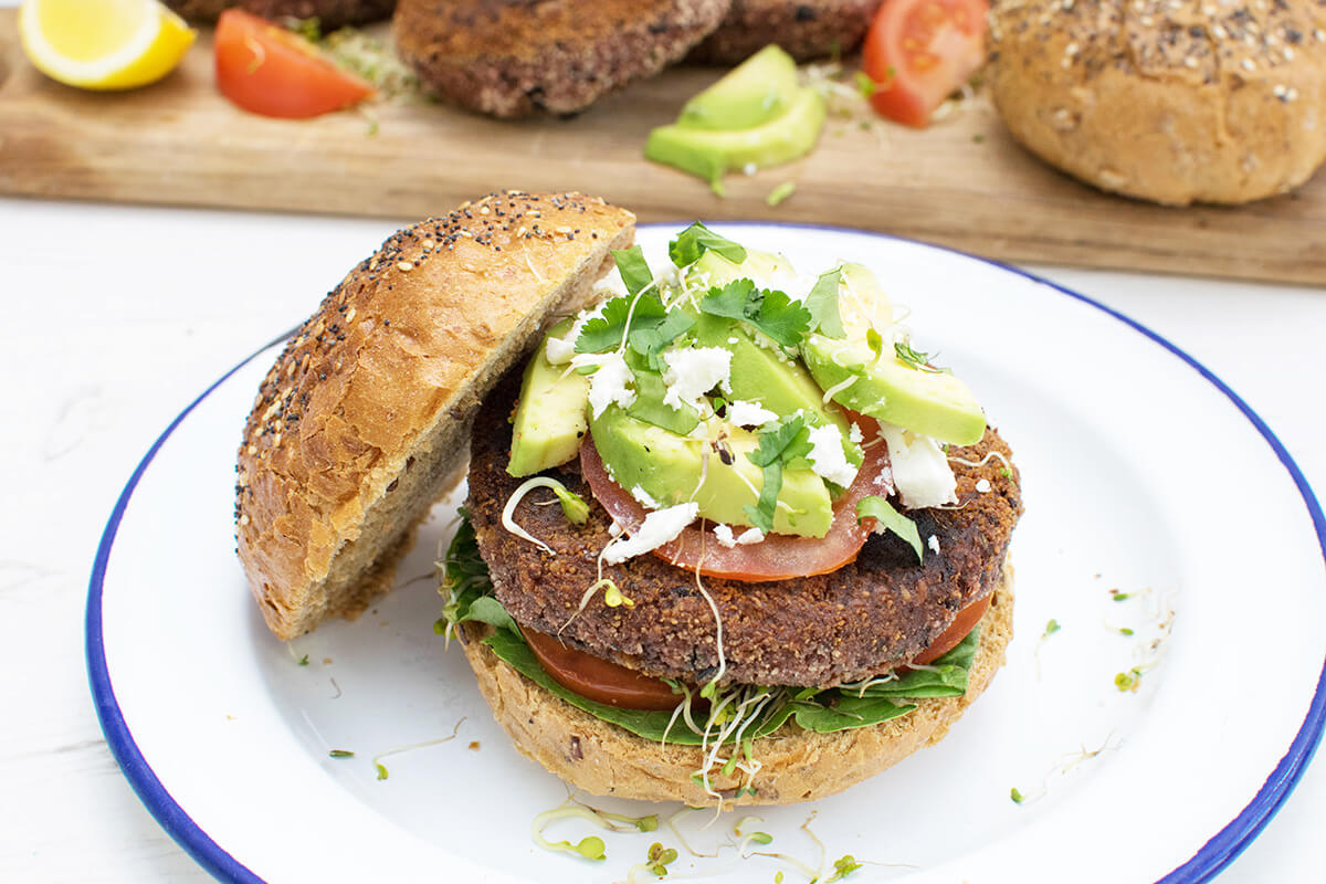 Beetroot burger in a seeded bun served with salad leaves, tomatoes, avocado and feta