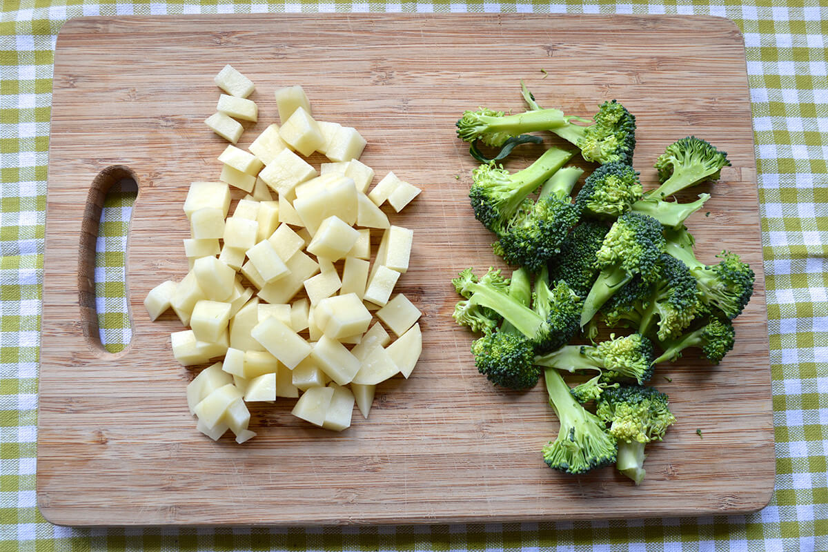 A wooden chopping board with diced potato and broccoli