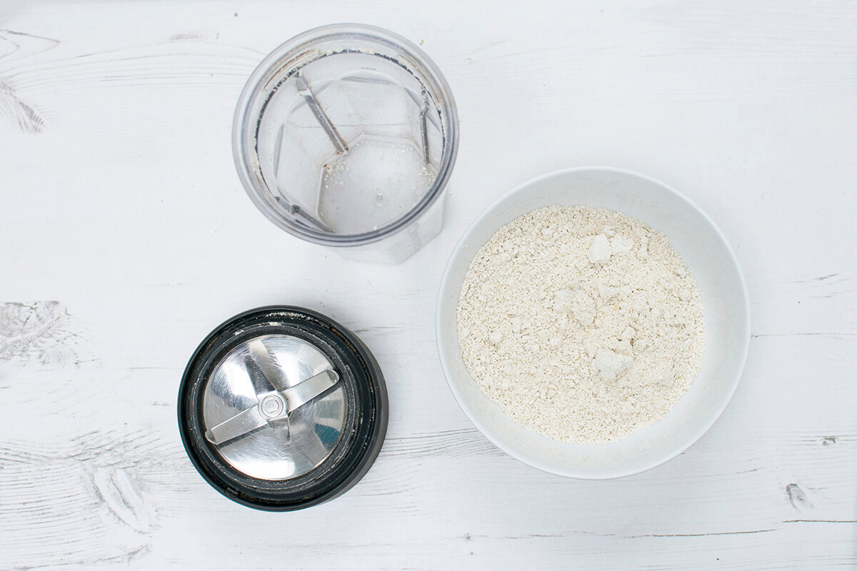 A bowl of oat flour next to a blender
