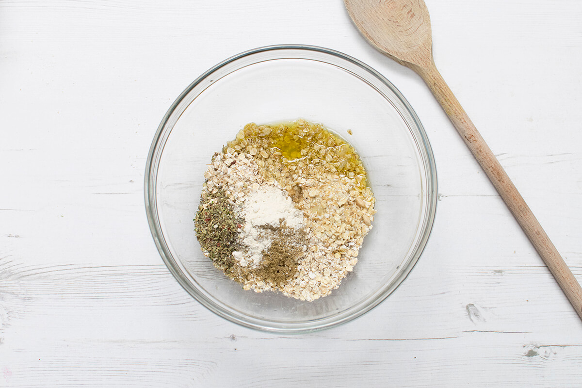 An a large bowl of oats with garlic powder, ground cumin, mixed dried herbs, oil and lemon juice