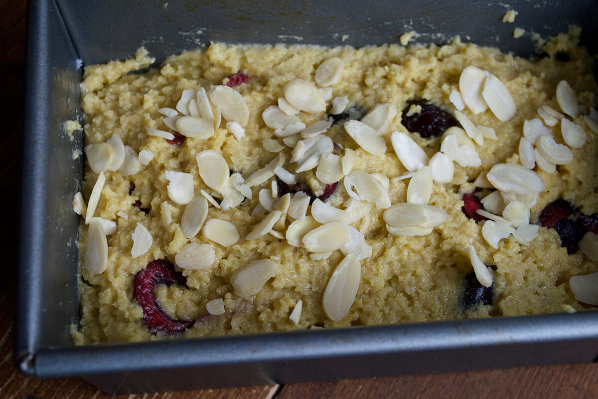 Uncooked cherry almond loaf dough in a loaf tin, topped with flaked almonds