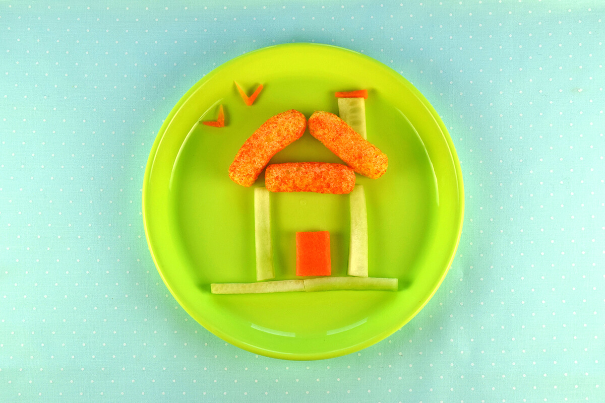 Rectangle of carrot placed within the cucumber square to create a door. V shaped carrot pieces placed above house to create birds 