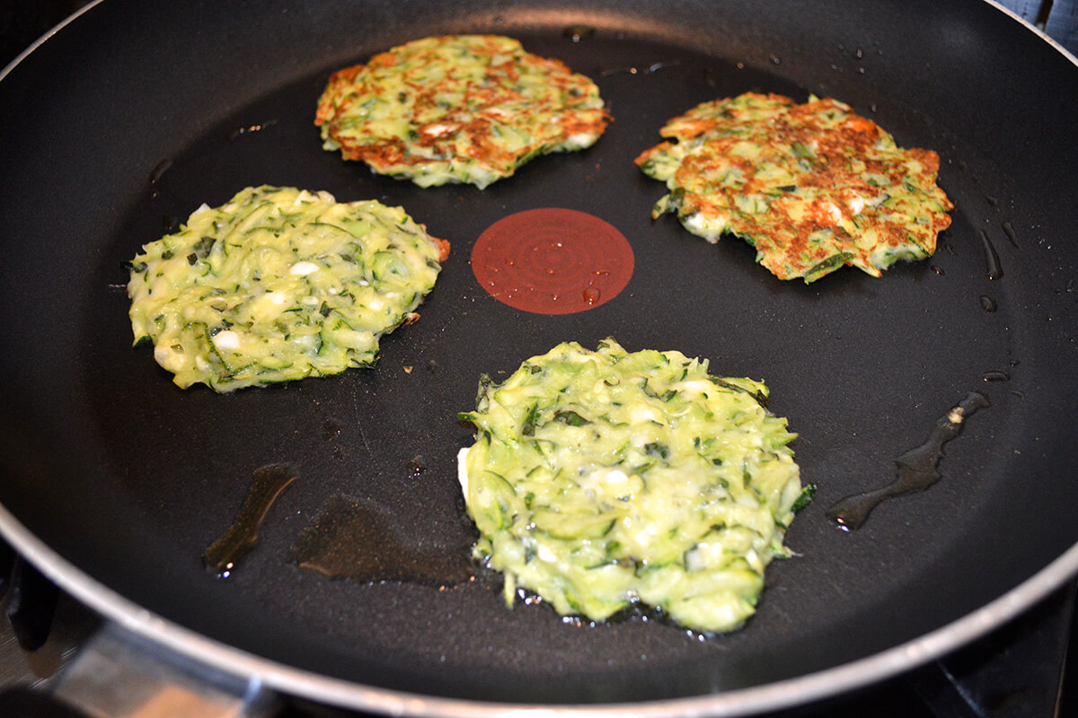 Courgette fritters being fried in frying pan