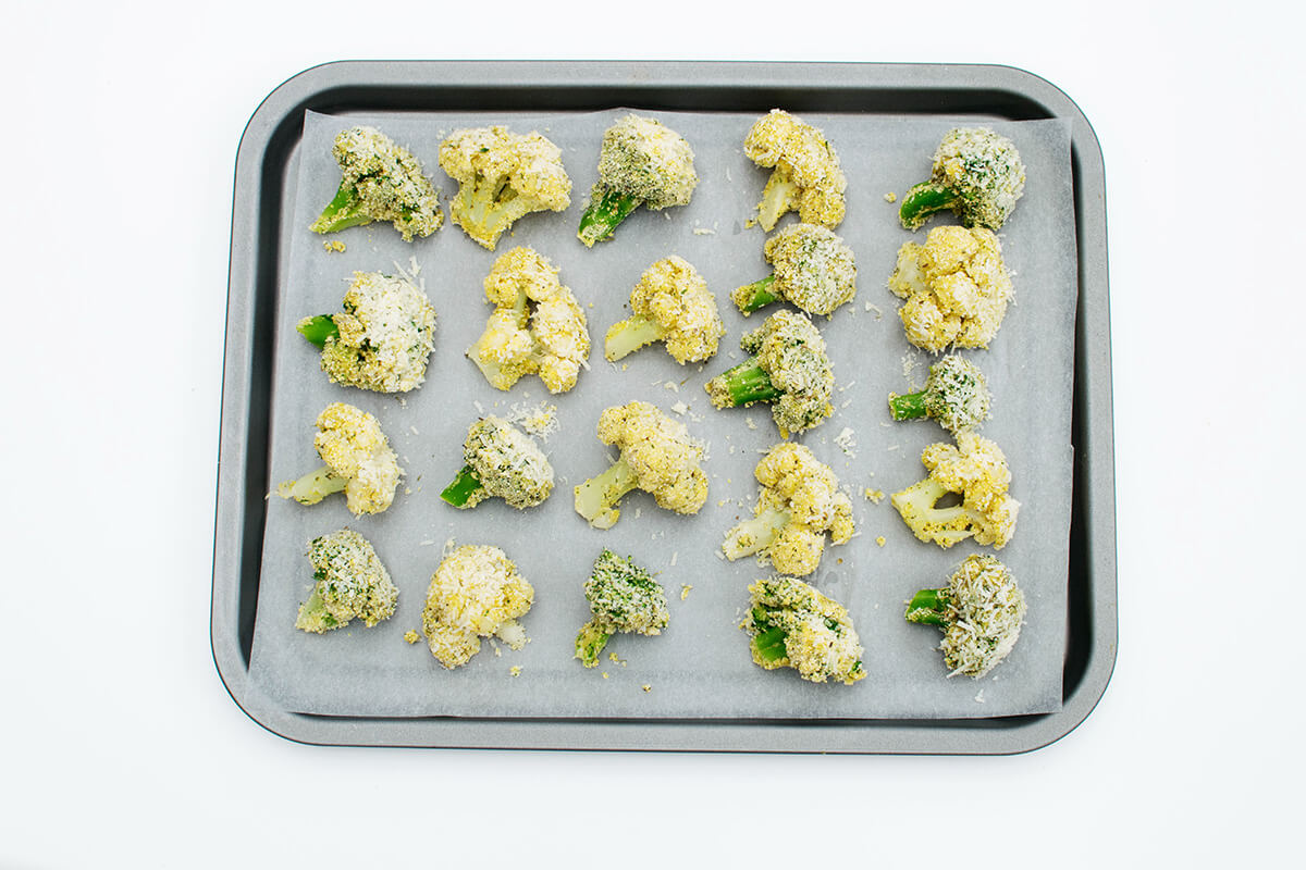 An oven tray of uncooked, coated cauliflower and broccoli florets