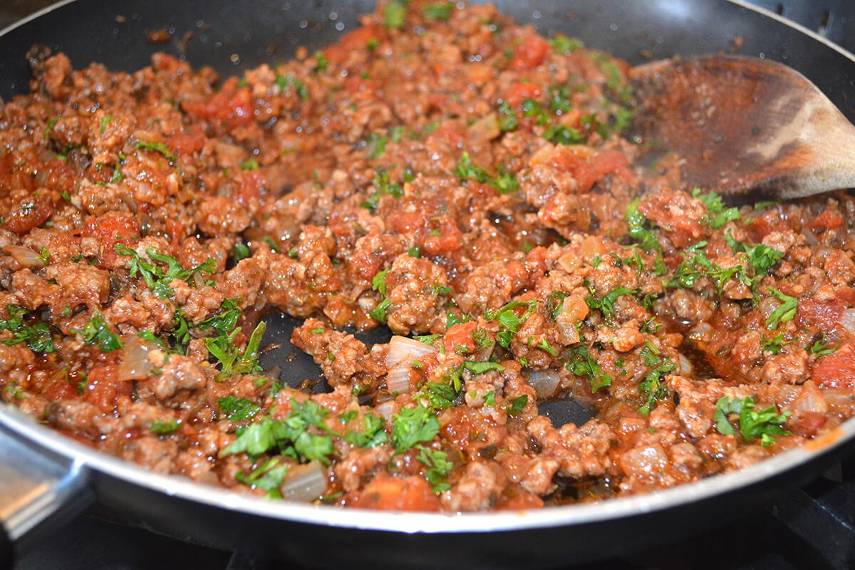 Lamb mince in a saucepan, being fried with onion and parsley