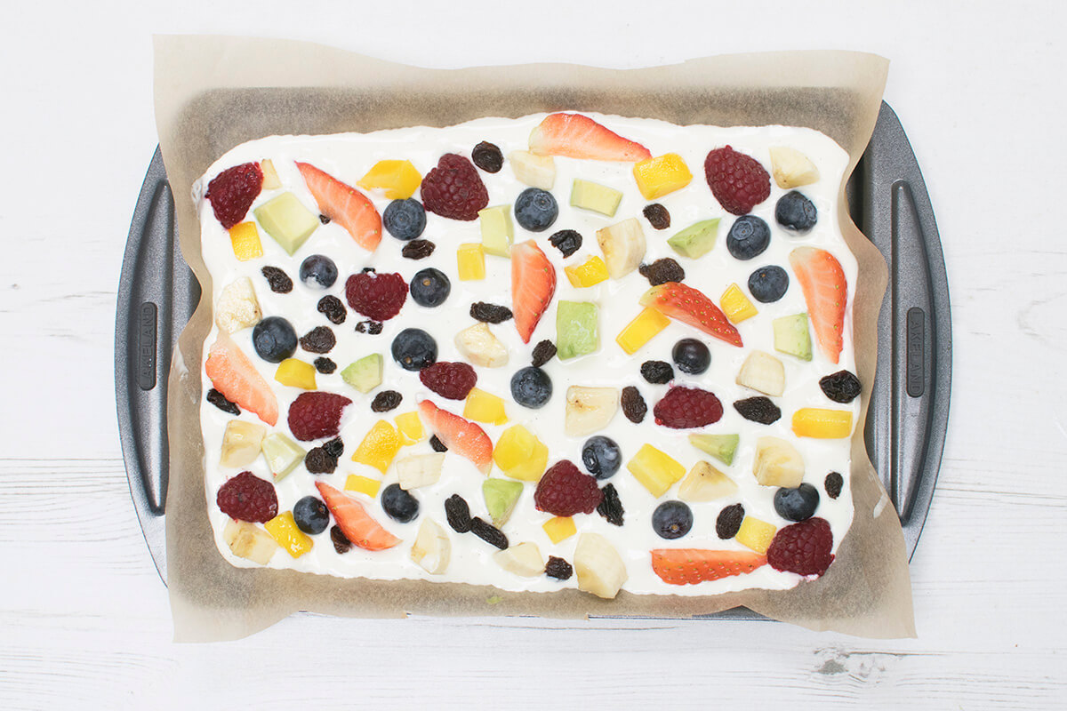A lined baking tray filled with yoghurt-vanilla mixture and topped with fruit
