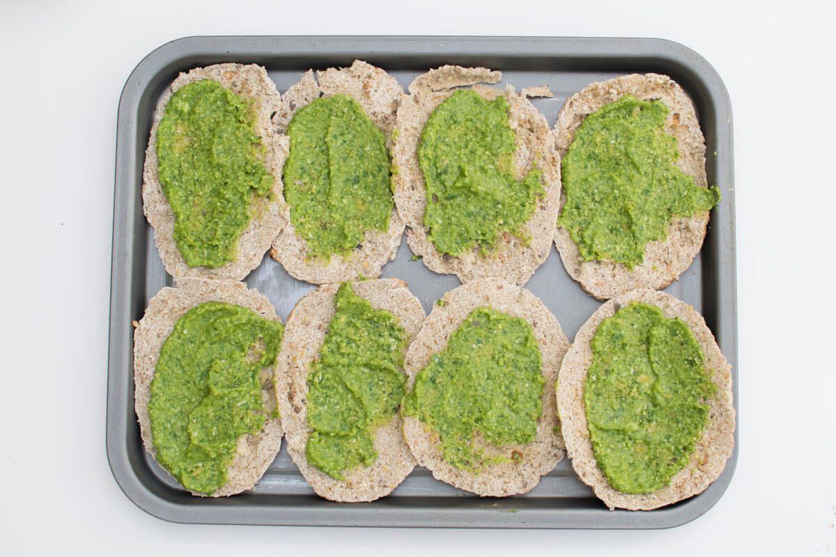 A baking tray with 4 halved pitta breads (8 halves) topped with green pesto