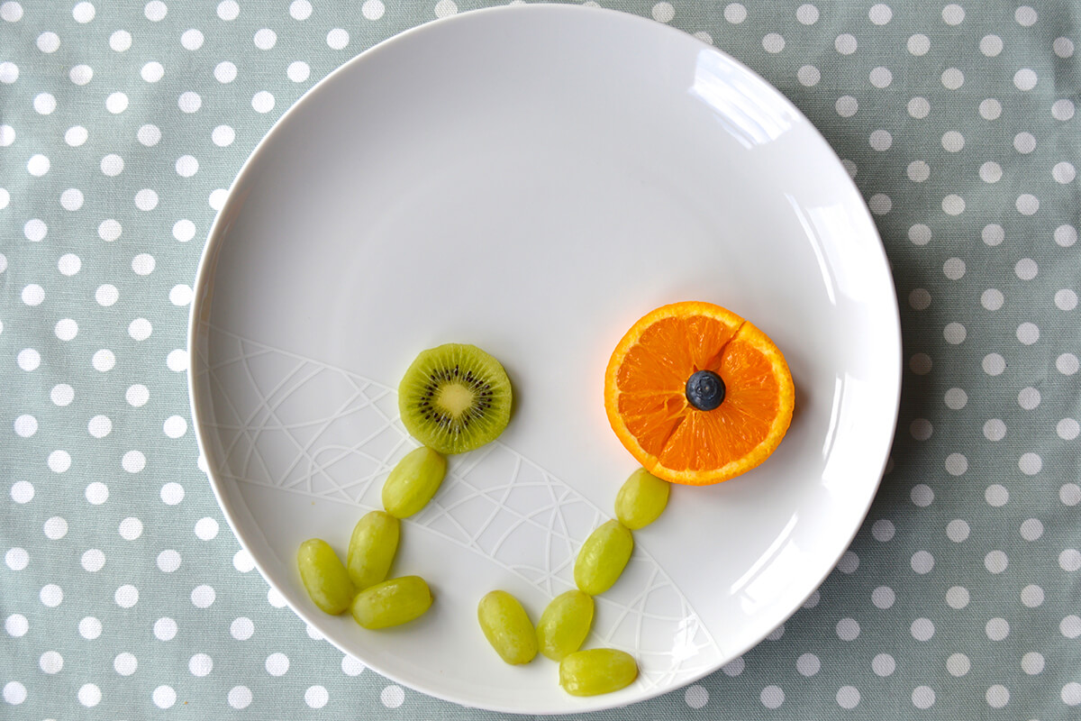 Circle kiwi fruit placed above on of the flower stems. Orange slices halved and placed above other flower stems with a blueberry in the centre