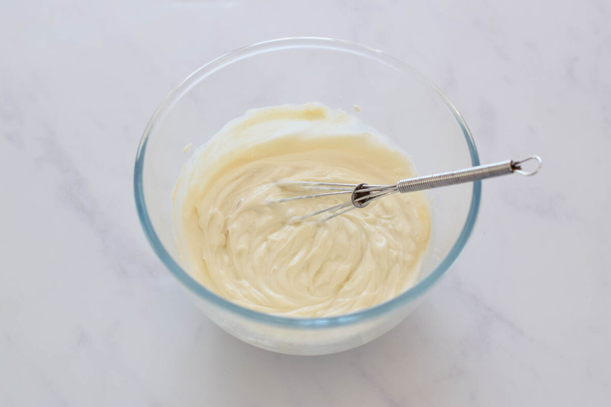 A glass bowl of maple yoghurt dip with a whisk in it