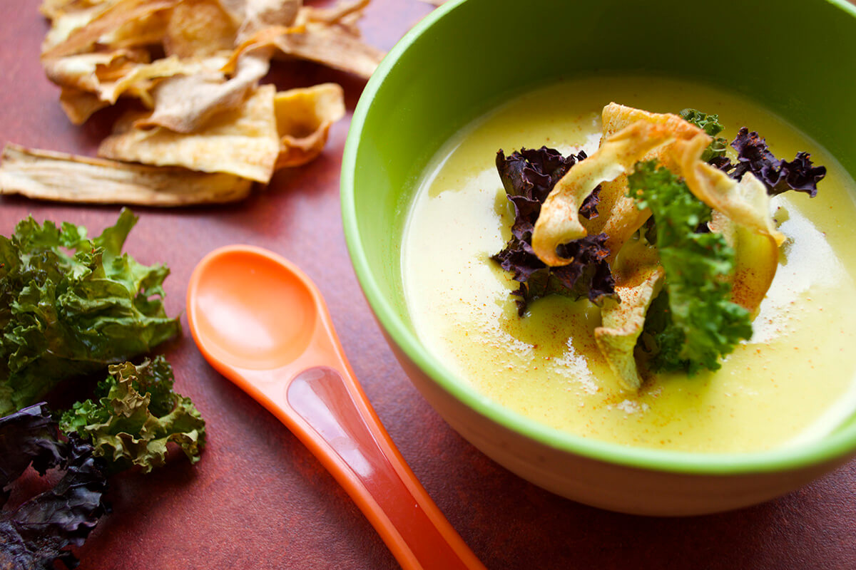 A bowl of Ginger & Butternut Soup next to some vegetable and kale crisps